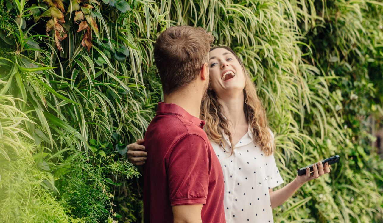 Jardinagem Vertical: Como ter um Jardim de Revista em Casa 31 Pessoas sorrindo e conversando com jardim vertical ao fundo.