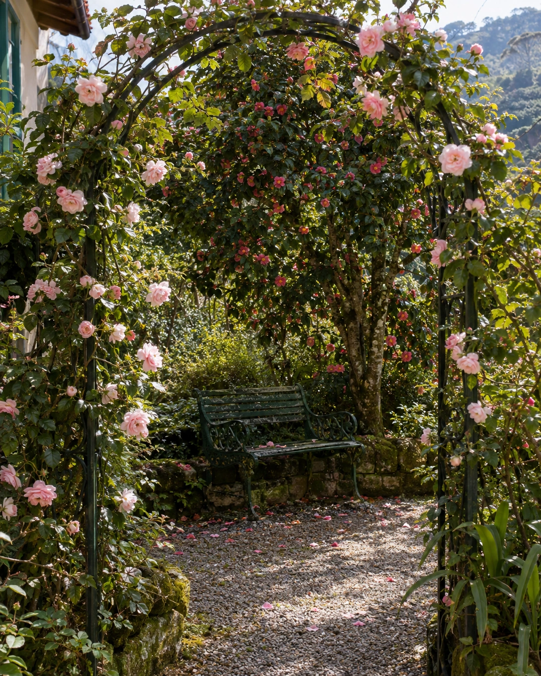 Jardim vintage: como criar um espaço romântico e acolhedor 2 Arco de ferro coberto por rosas cor-de-rosa em flor, conduzindo o olhar até um banco vintage sob a copa de uma árvore.